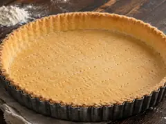Base de masa para tarta dulce horneada a ciegas en molde acanalado, dorada y pinchada con tenedor, sobre mesa de madera oscura